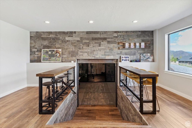 bar area with wood finished floors, a multi sided fireplace, baseboards, and recessed lighting