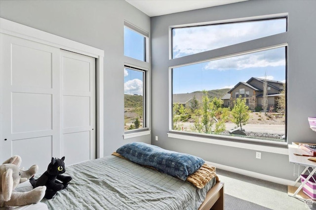 carpeted bedroom with multiple windows, a closet, and baseboards