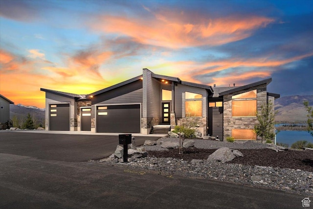 contemporary home with stone siding, a garage, and driveway
