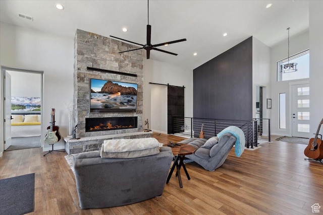living area with high vaulted ceiling, a stone fireplace, ceiling fan, wood finished floors, and a barn door