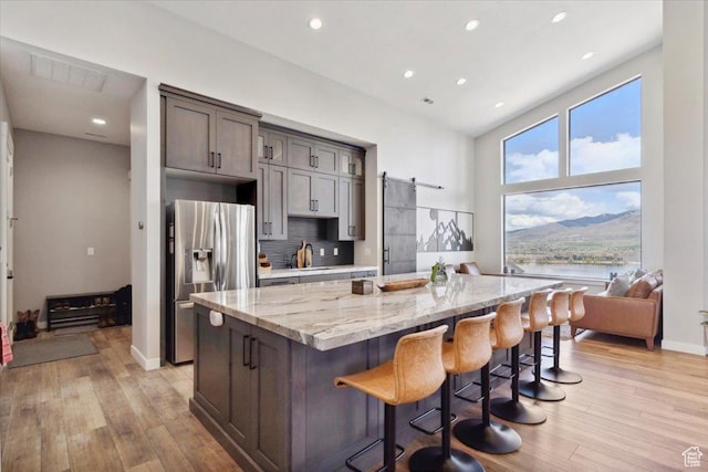 kitchen with stainless steel refrigerator with ice dispenser, a center island, light stone countertops, light wood-style floors, and recessed lighting