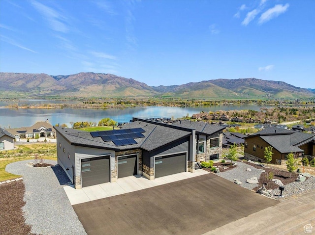 view of front of home with a garage, concrete driveway, a water and mountain view, and roof mounted solar panels