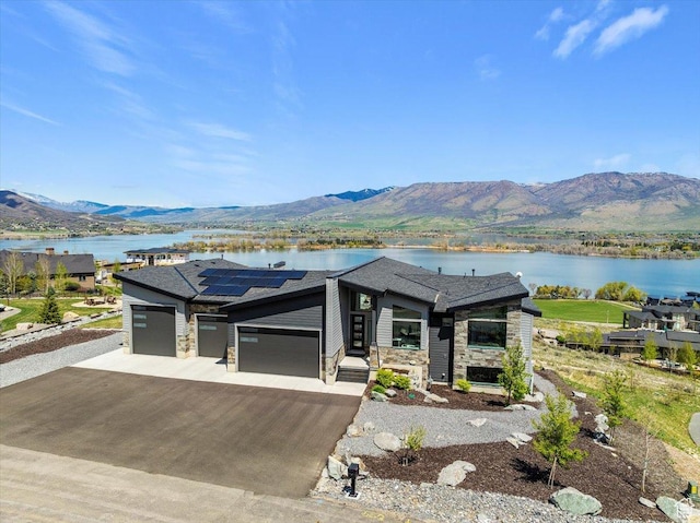 view of front of house featuring stone siding, a garage, driveway, roof mounted solar panels, and a water and mountain view