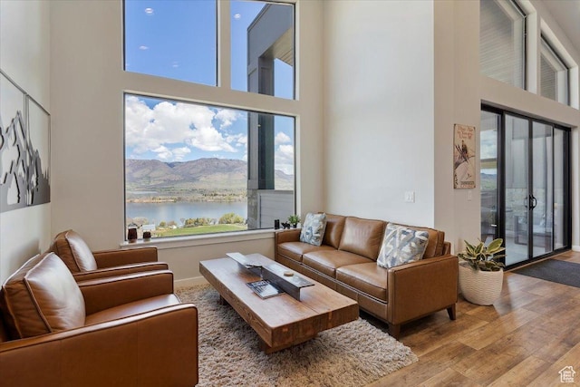 living area featuring a towering ceiling, wood finished floors, and a water and mountain view