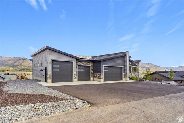 view of front of house with a mountain view, driveway, solar panels, an attached garage, and stone siding