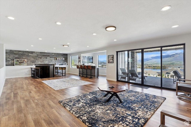 living room featuring wood finished floors, a textured ceiling, recessed lighting, baseboards, and a water view