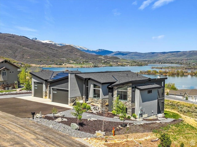 view of front of property featuring a garage, stone siding, a water and mountain view, and driveway