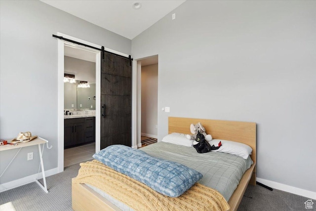 bedroom with a barn door, vaulted ceiling, baseboards, light colored carpet, and connected bathroom