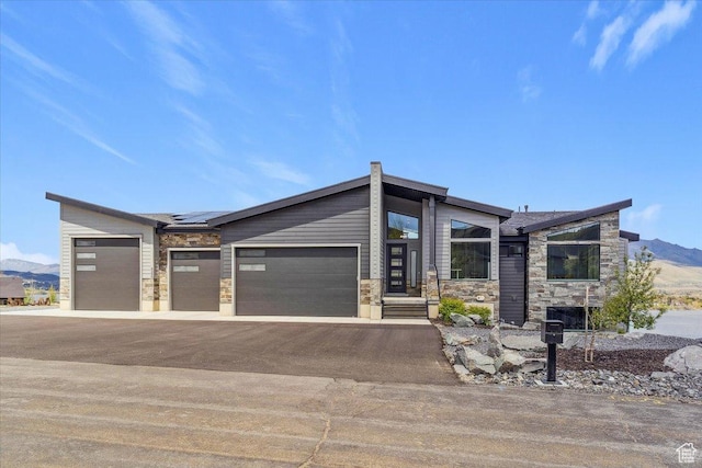 contemporary house featuring stone siding, solar panels, driveway, a garage, and a mountain view