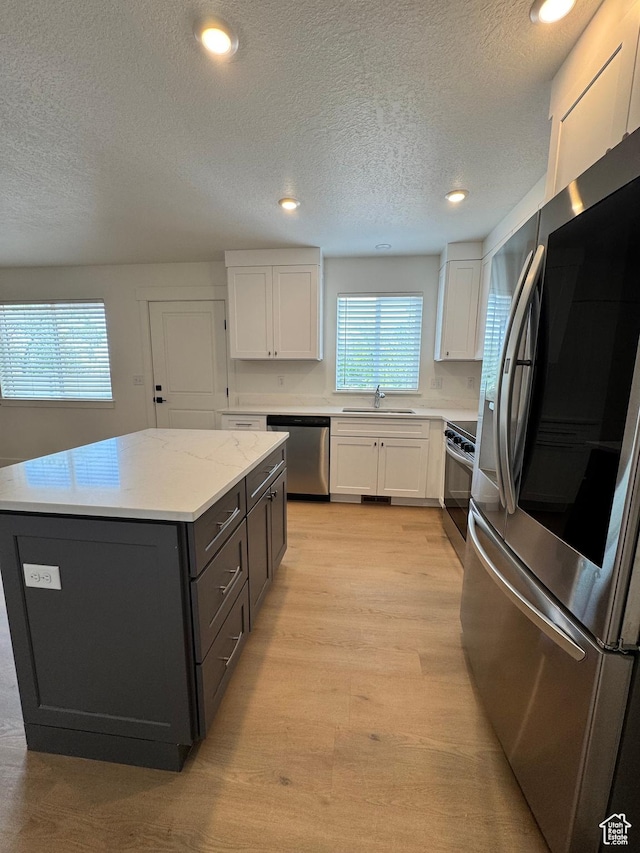kitchen featuring appliances with stainless steel finishes, a sink, white cabinets, a textured ceiling, and a kitchen island
