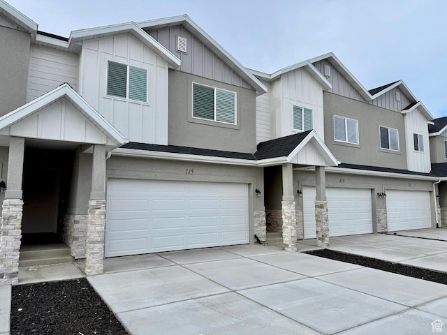 multi unit property with board and batten siding, an attached garage, stone siding, and concrete driveway
