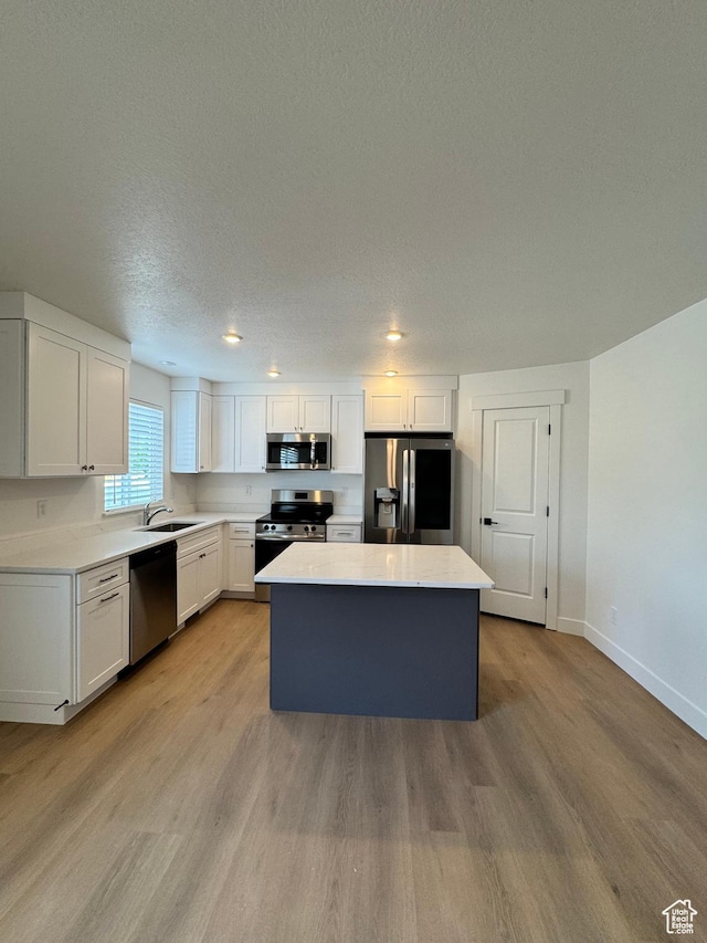 kitchen with appliances with stainless steel finishes, a kitchen island, light wood finished floors, baseboards, and a textured ceiling