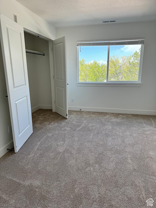 unfurnished bedroom featuring carpet floors, baseboards, a textured ceiling, and a closet