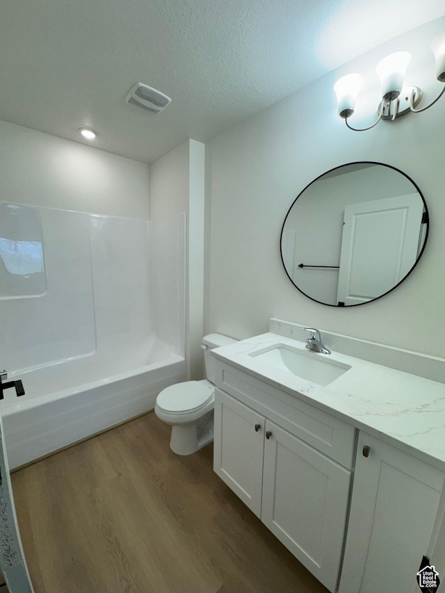 bathroom with wood finished floors, vanity, toilet, a textured ceiling, and tub / shower combination