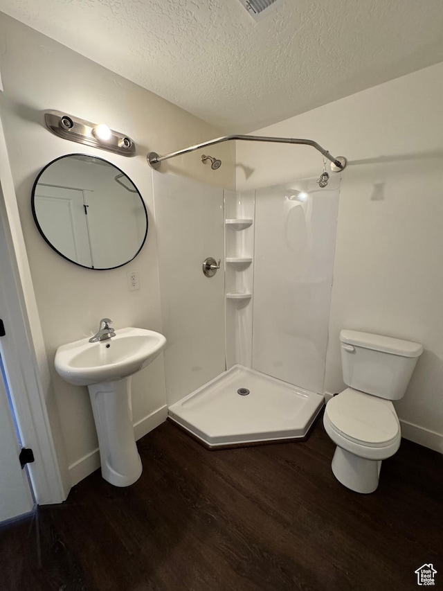 full bath with wood finished floors, a stall shower, a textured ceiling, baseboards, and toilet