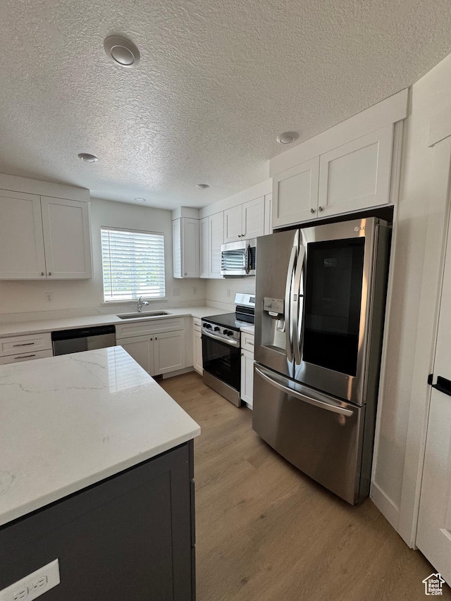 kitchen featuring stainless steel appliances, a sink, light wood finished floors, white cabinetry, and a textured ceiling