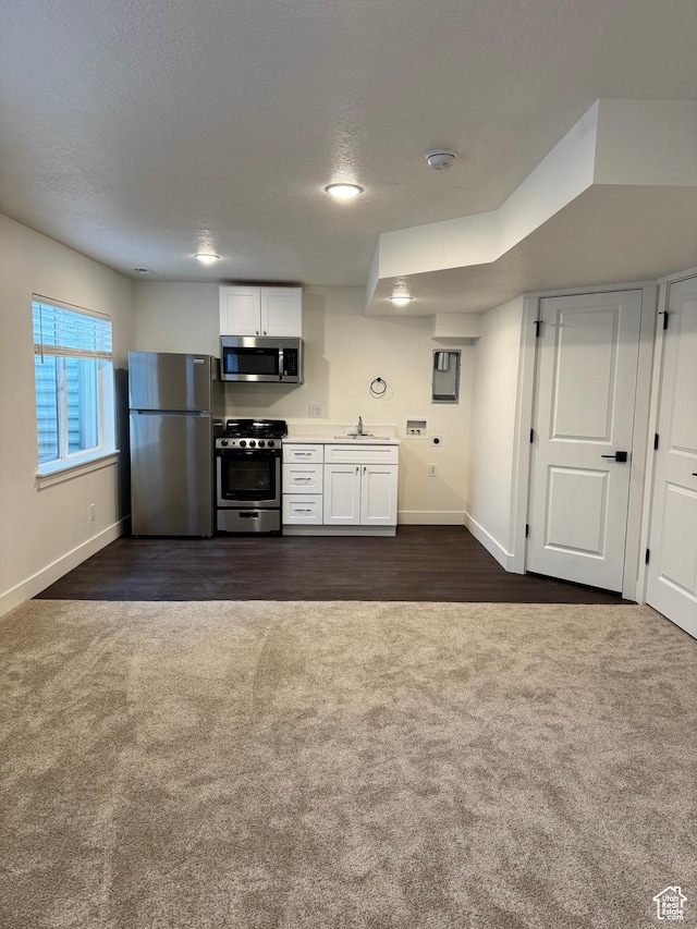 kitchen featuring stainless steel appliances, dark colored carpet, a sink, baseboards, and a textured ceiling