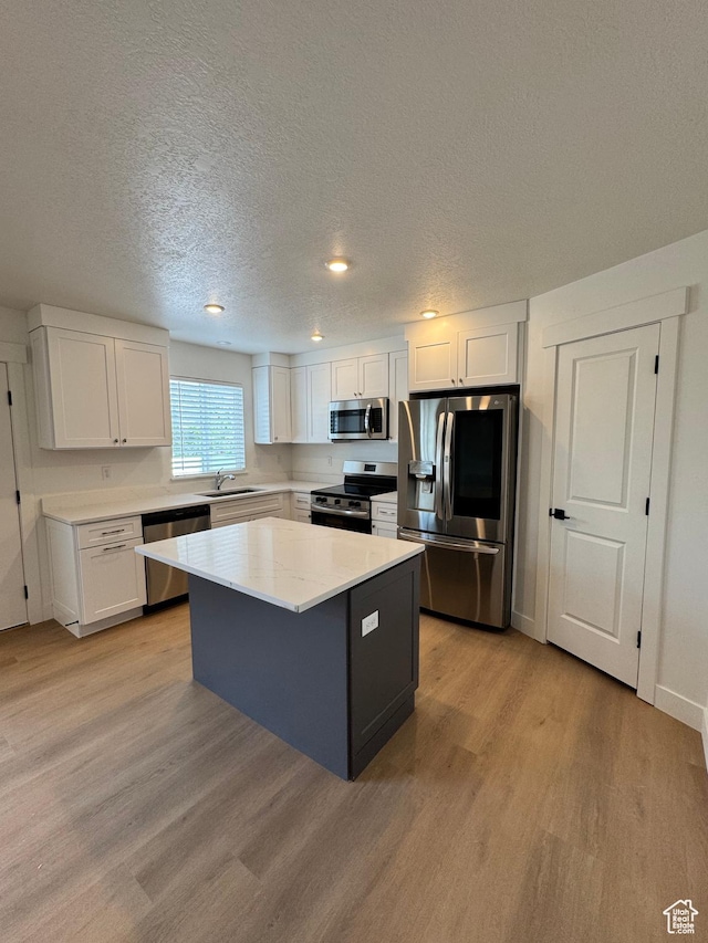 kitchen featuring stainless steel appliances, a sink, light wood-style flooring, a textured ceiling, and white cabinets