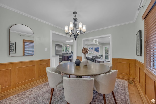dining area with a wainscoted wall, light wood-style floors, a chandelier, and crown molding