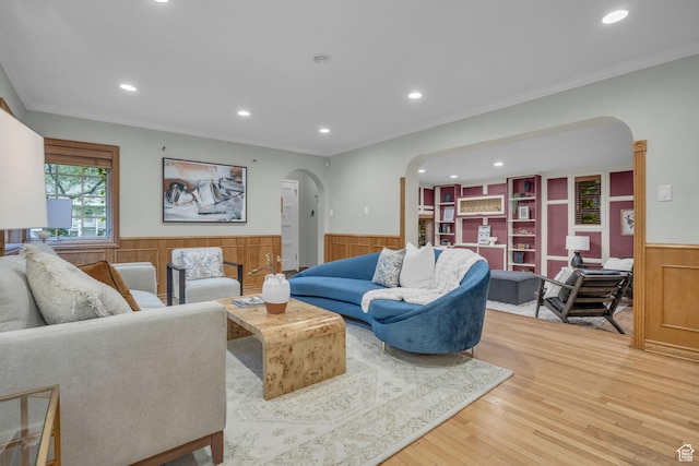 living room with arched walkways, a wainscoted wall, recessed lighting, light wood-style flooring, and crown molding