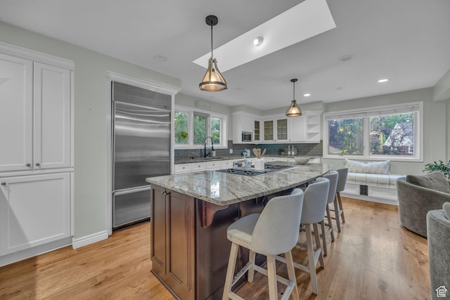 kitchen with appliances with stainless steel finishes, a sink, white cabinetry, light stone countertops, and decorative backsplash