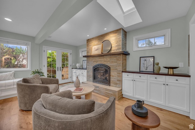 living room featuring a skylight, a fireplace, light wood-style flooring, french doors, and beam ceiling