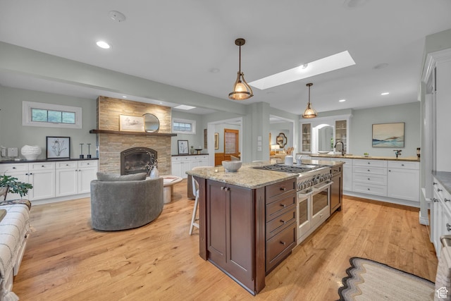 kitchen featuring a stone fireplace, white cabinets, light wood-style flooring, and recessed lighting