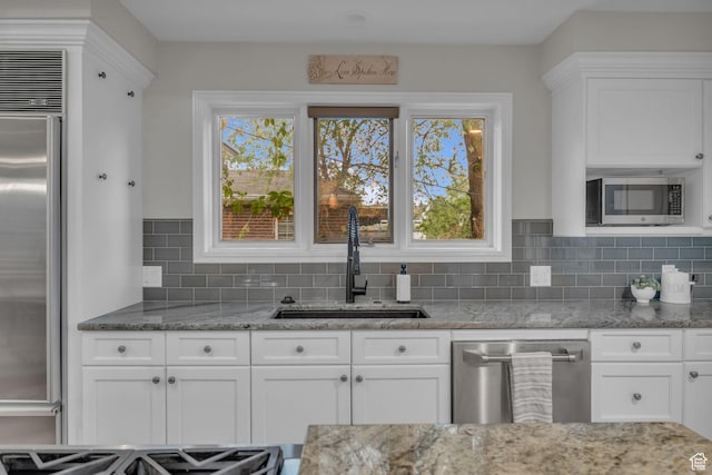 kitchen featuring a sink, appliances with stainless steel finishes, tasteful backsplash, white cabinetry, and light stone counters