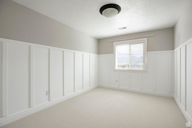 empty room featuring a decorative wall, light carpet, and wainscoting