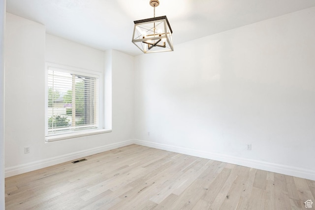 empty room featuring a chandelier, baseboards, and light wood-style floors