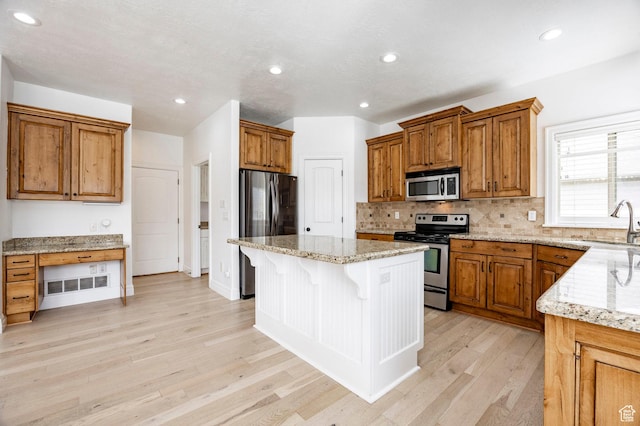 kitchen with appliances with stainless steel finishes, a sink, a kitchen bar, light wood-style floors, and backsplash