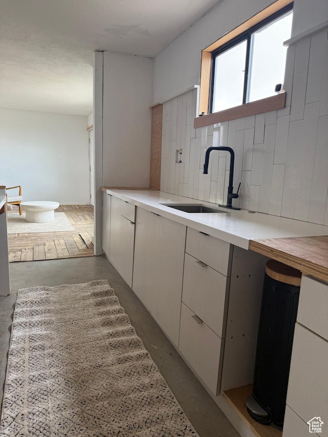 kitchen featuring a sink, light countertops, concrete flooring, and decorative backsplash