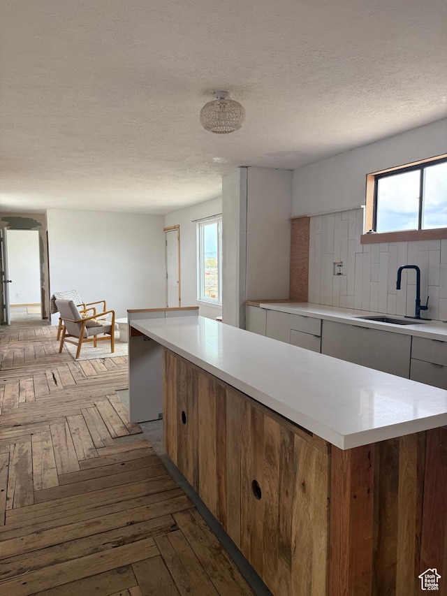 kitchen featuring a sink, light countertops, plenty of natural light, parquet flooring, and a textured ceiling