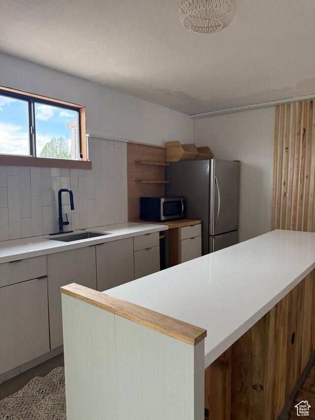 kitchen featuring appliances with stainless steel finishes, a sink, light countertops, decorative backsplash, and a textured ceiling