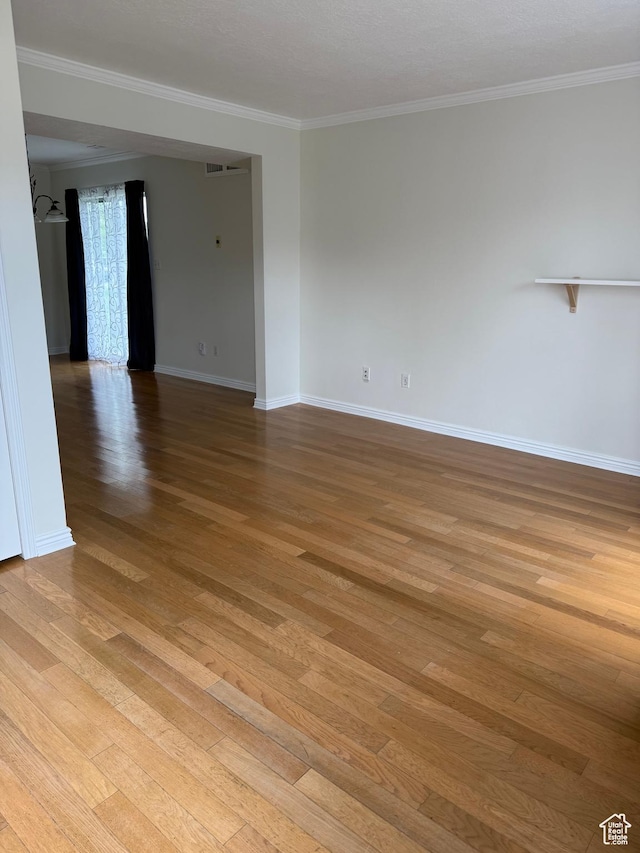 empty room with light wood-type flooring, crown molding, and baseboards
