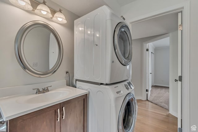 laundry room with stacked washer and clothes dryer, a sink, light wood-style floors, and baseboards