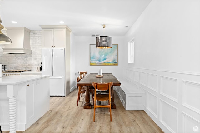 dining area featuring light wood-type flooring, a decorative wall, a wainscoted wall, and recessed lighting