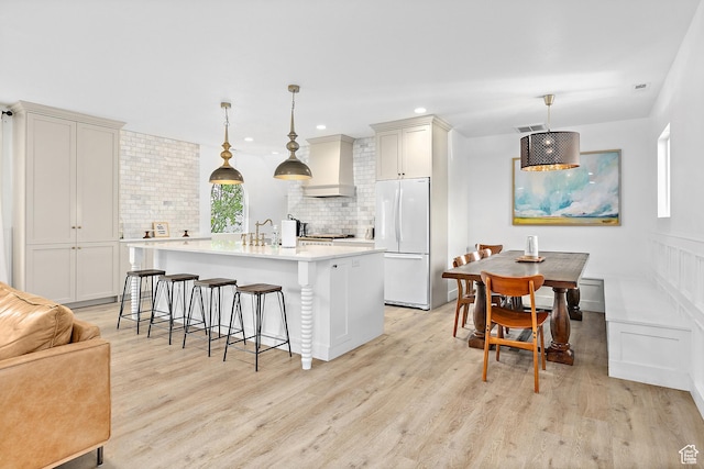 kitchen featuring freestanding refrigerator, wall chimney exhaust hood, light wood finished floors, a breakfast bar, and decorative backsplash