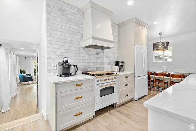 kitchen featuring white appliances, wall chimney range hood, healthy amount of natural light, light wood-style floors, and recessed lighting
