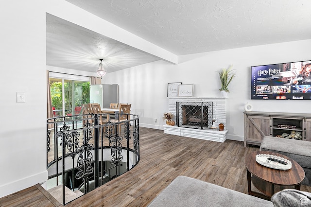 living room with a fireplace, baseboards, wood finished floors, beamed ceiling, and a textured ceiling