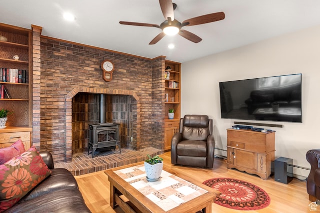 living room with a wood stove, a ceiling fan, light wood-style floors, and a baseboard heating unit