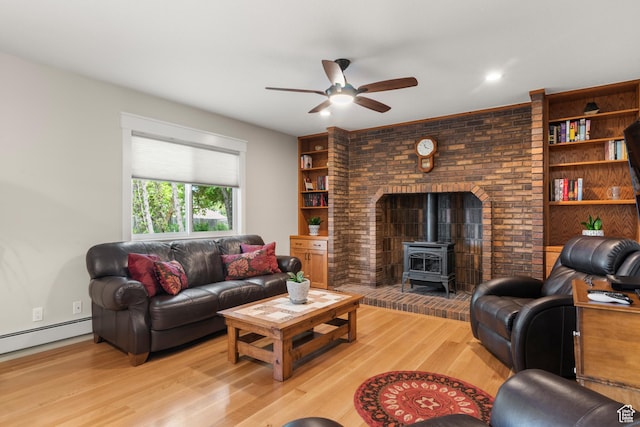 living room featuring a wood stove, ceiling fan, light wood finished floors, and a baseboard heating unit