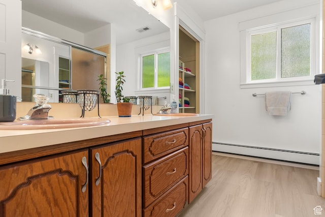 full bath featuring a baseboard heating unit, an enclosed shower, double vanity, and wood finished floors