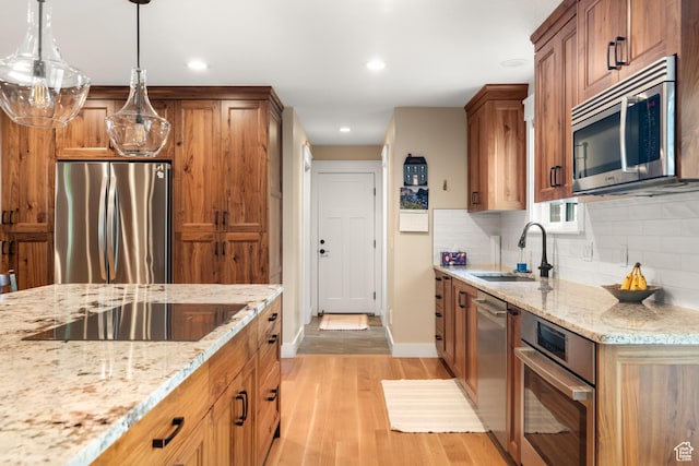 kitchen featuring appliances with stainless steel finishes, light wood-style flooring, a sink, brown cabinetry, and light stone countertops