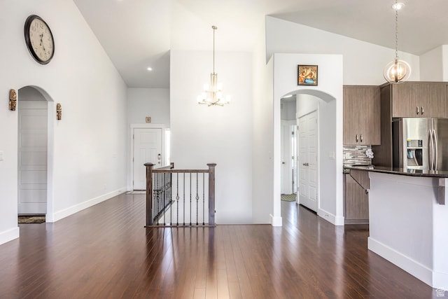 kitchen with arched walkways, stainless steel fridge with ice dispenser, a chandelier, dark wood finished floors, and high vaulted ceiling