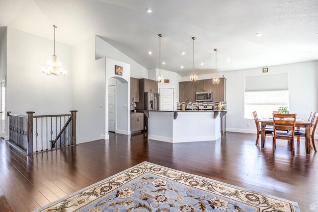 kitchen with appliances with stainless steel finishes, a breakfast bar, dark wood finished floors, a chandelier, and lofted ceiling