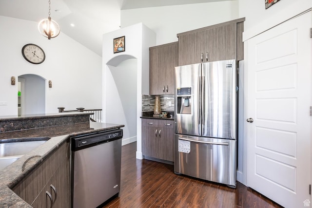 kitchen featuring appliances with stainless steel finishes, arched walkways, backsplash, dark wood-style flooring, and dark stone countertops
