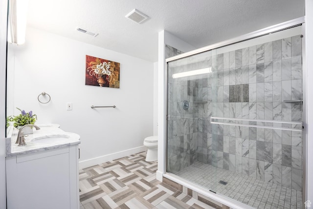 bathroom with a stall shower, toilet, baseboards, double vanity, and a textured ceiling