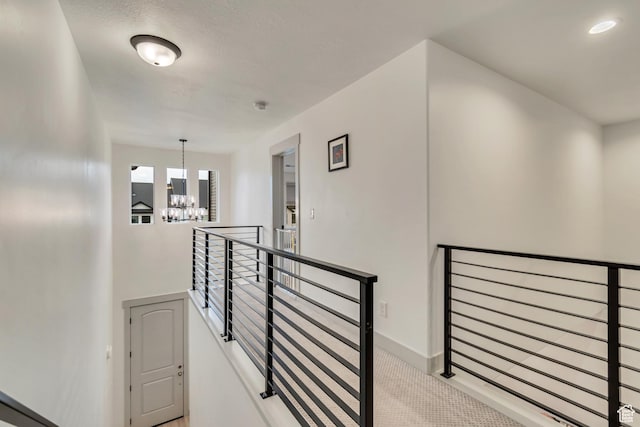 hall with an upstairs landing, a chandelier, carpet floors, and baseboards