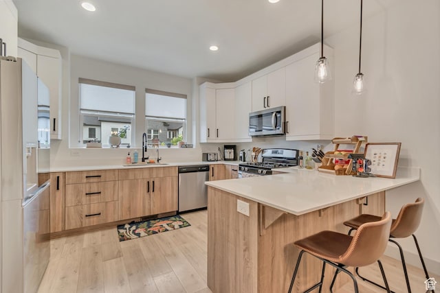 kitchen with appliances with stainless steel finishes, a sink, light wood finished floors, a peninsula, and light countertops